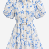 A white eyelet mini dress with a blue floral print, featuring puff sleeves, a pointed collar, and a matching waist tie with a gold buckle.