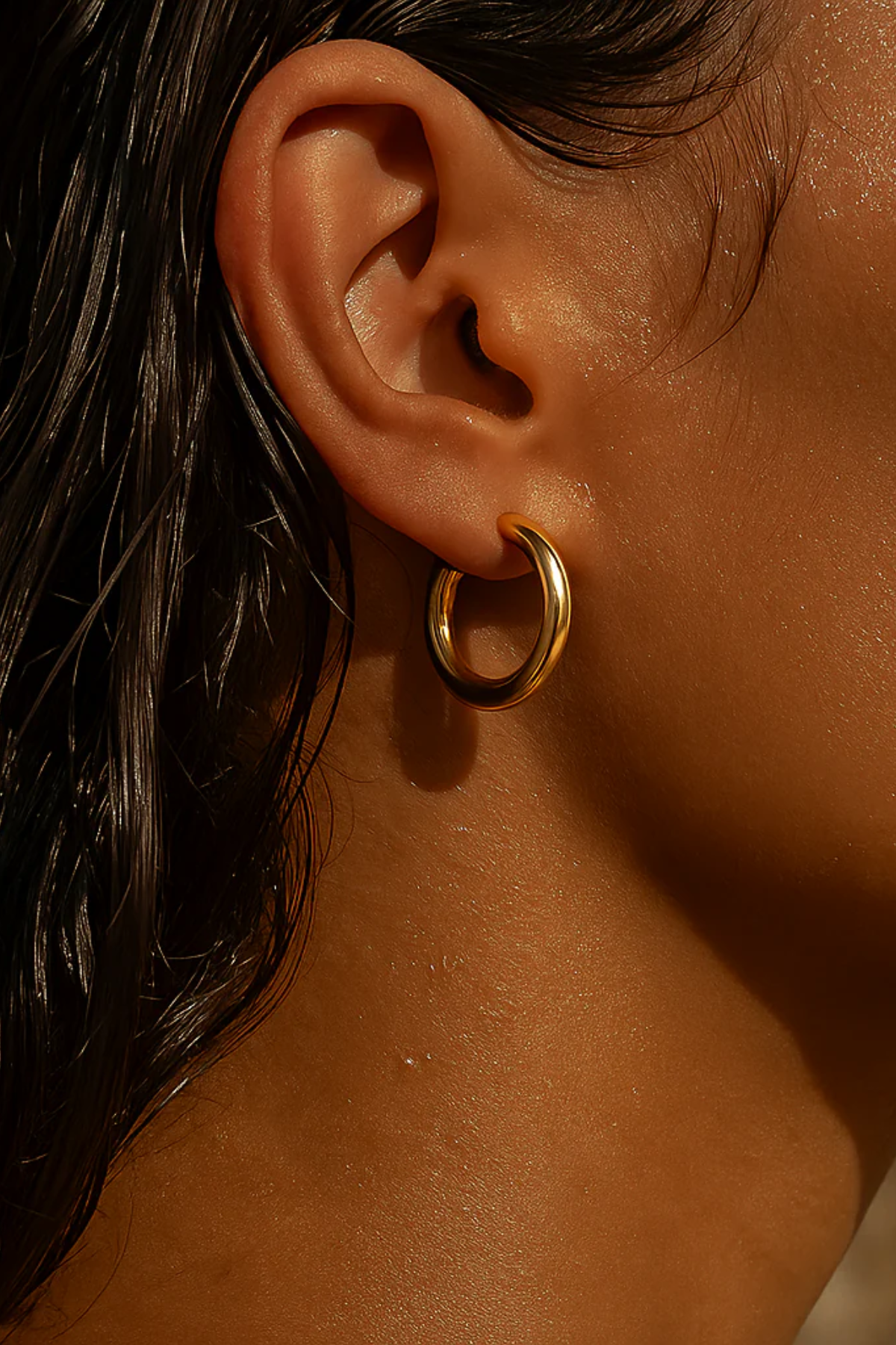 Close-up of an ear wearing a gold hoop earring with a blurred background