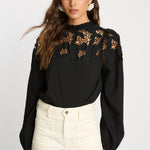 Woman wearing a black blouse with floral lace details on a white background