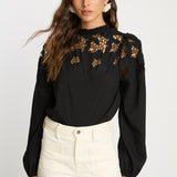 Woman wearing a black blouse with floral lace details on a white background
