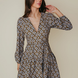 A woman modeling a long-sleeve mini dress with a brown, beige, and white geometric pattern against a solid beige background.