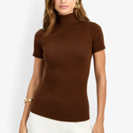 A woman modeling a short-sleeve ribbed mock neck top in dark brown, paired with white pants, against a plain white background.