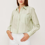 Woman wearing a light green button-up shirt and white pants against a plain background