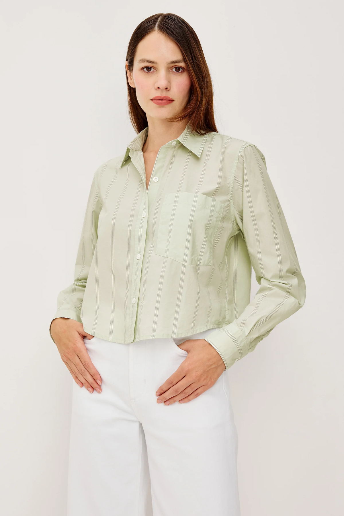Woman wearing a light green button-up shirt and white pants against a plain background