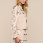 Woman wearing a beige blazer over a white lace dress on a beige background