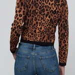 A person shown from the back wearing a cropped long-sleeve knit top with a brown and black leopard print, paired with blue jeans, against a light gray studio background.