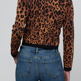 A person shown from the back wearing a cropped long-sleeve knit top with a brown and black leopard print, paired with blue jeans, against a light gray studio background.