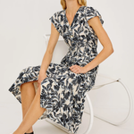 Woman wearing a black and white floral dress sitting on a white chair against a white background
