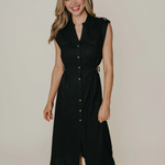 Model wearing a sleeveless black midi dress with a tailored silhouette and subtle front detailing, photographed against a neutral studio background.
