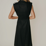Model wearing a sleeveless black midi dress with a tailored silhouette and subtle front detailing, photographed against a neutral studio background.