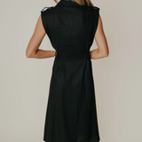 Model wearing a sleeveless black midi dress with a tailored silhouette and subtle front detailing, photographed against a neutral studio background.