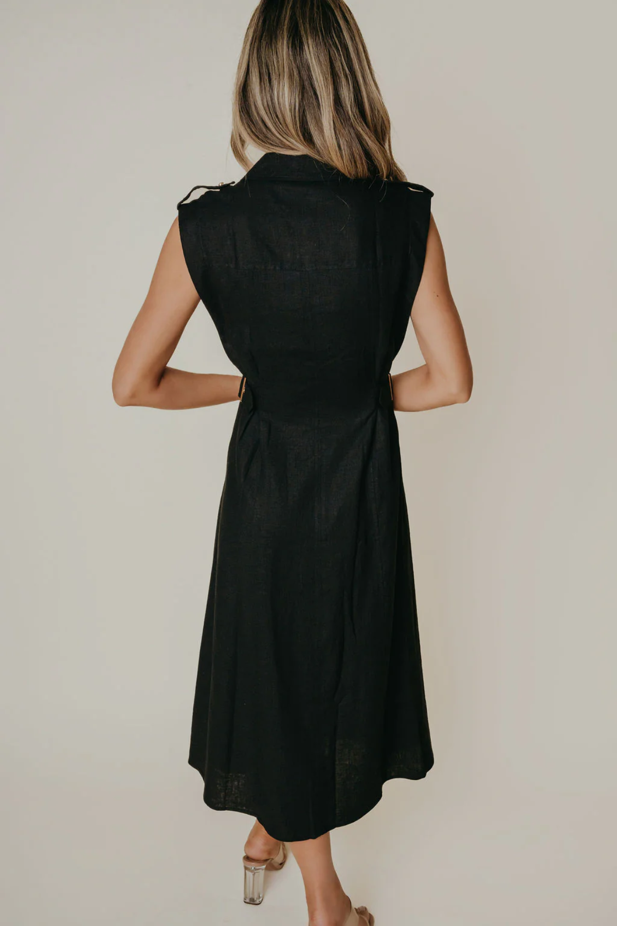 Model wearing a sleeveless black midi dress with a tailored silhouette and subtle front detailing, photographed against a neutral studio background.