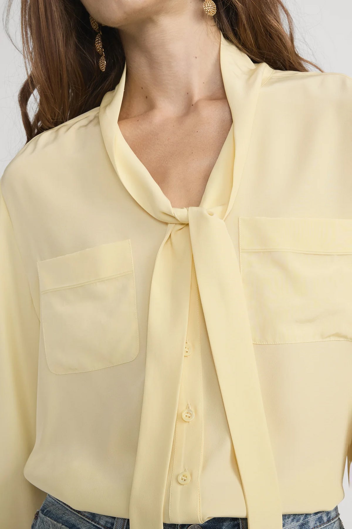 Yellow blouse with a tie detail worn by a person, on a plain background