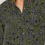 Close-up of a person wearing an olive green button-up shirt with a black and white animal print pattern.