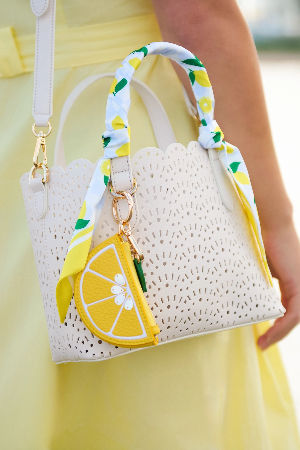 White woven handbag with lemon charm and decorative strap, held by a person in a yellow dress.