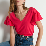Woman wearing a red blouse and blue jeans against a plain background
