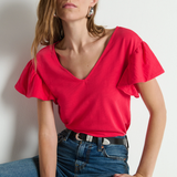 Woman wearing a red blouse and blue jeans against a plain background