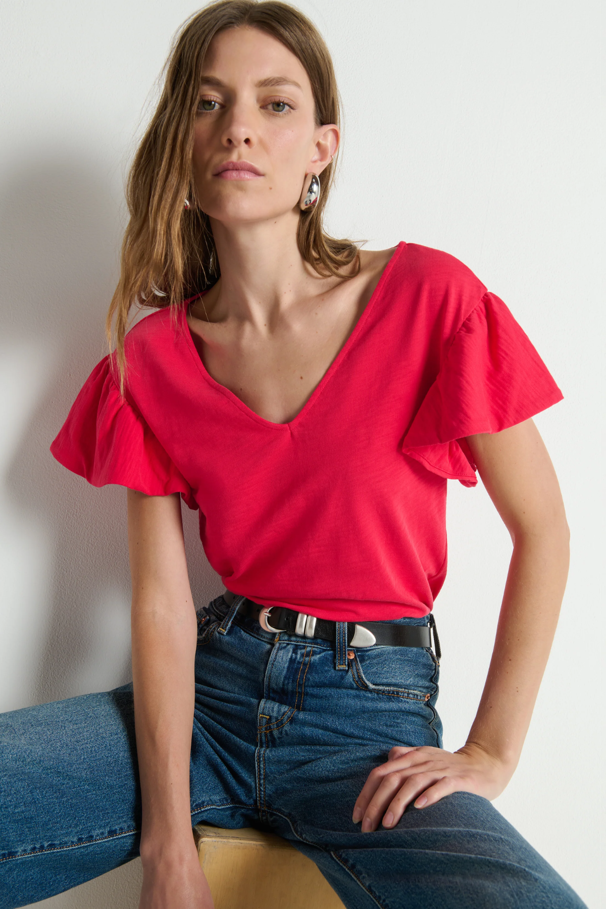 Woman wearing a red blouse and blue jeans against a plain background
