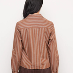 A woman viewed from behind wearing a brown and beige vertically striped long-sleeve shirt and a dark brown skirt, set against a plain white background.