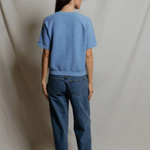 Person wearing a blue t-shirt and jeans standing against a plain background