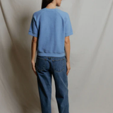 Person wearing a blue t-shirt and jeans standing against a plain background