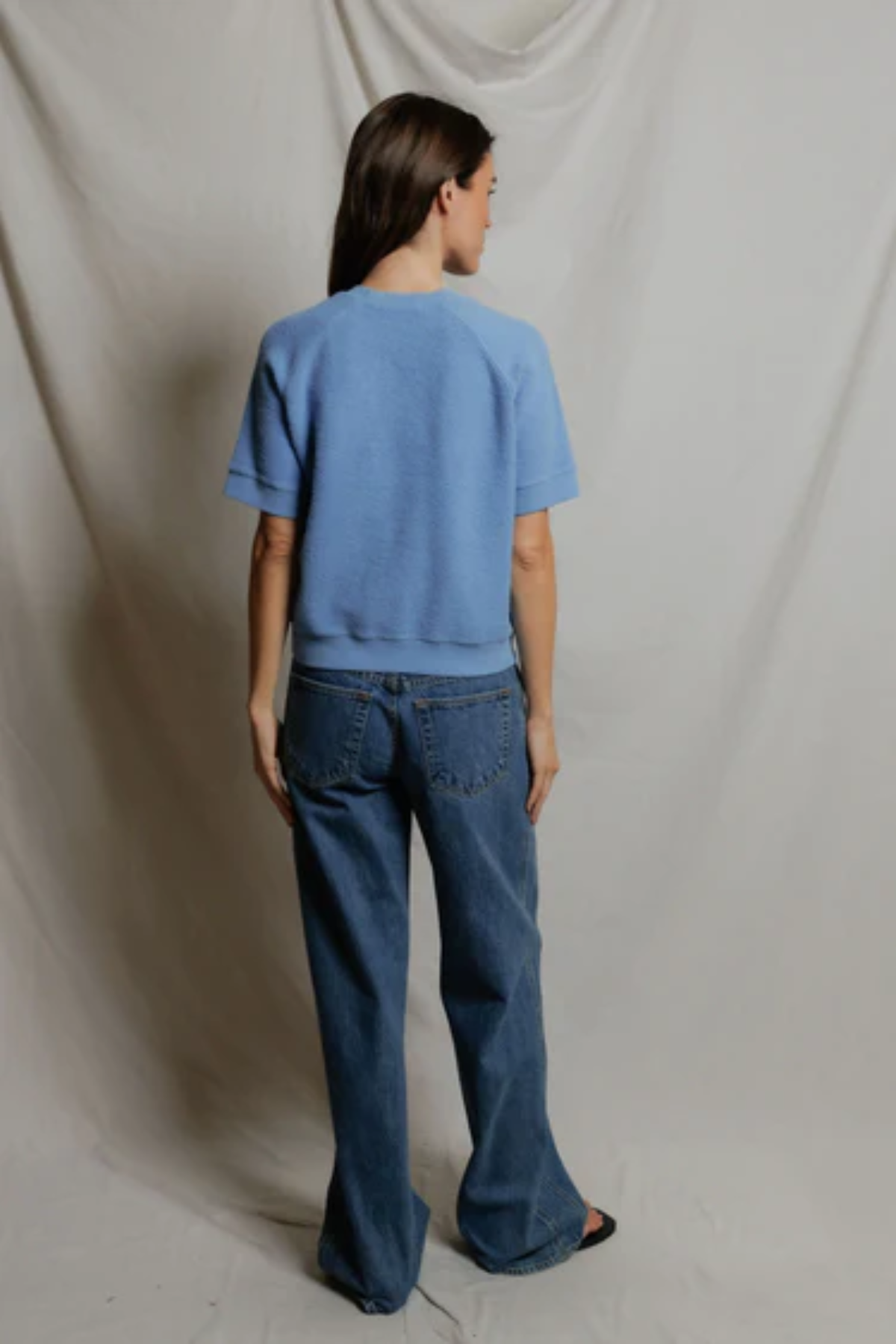 Person wearing a blue t-shirt and jeans standing against a plain background
