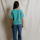 Person wearing a teal shirt and blue jeans standing against a plain white background