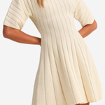 A woman wearing a cream-colored short-sleeve ribbed knit dress with a flared skirt, shown against a plain light background.