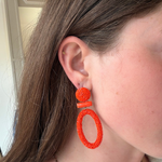 Bright orange beaded statement earrings displayed on a model.