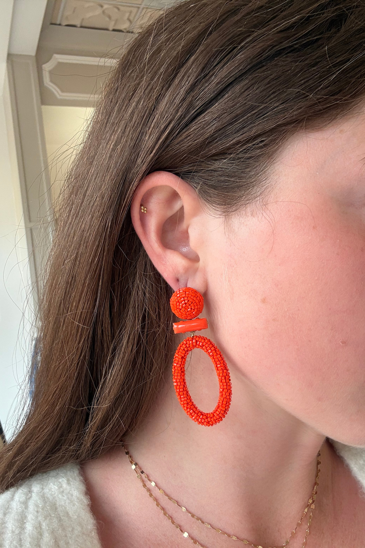 Bright orange beaded statement earrings displayed on a model.