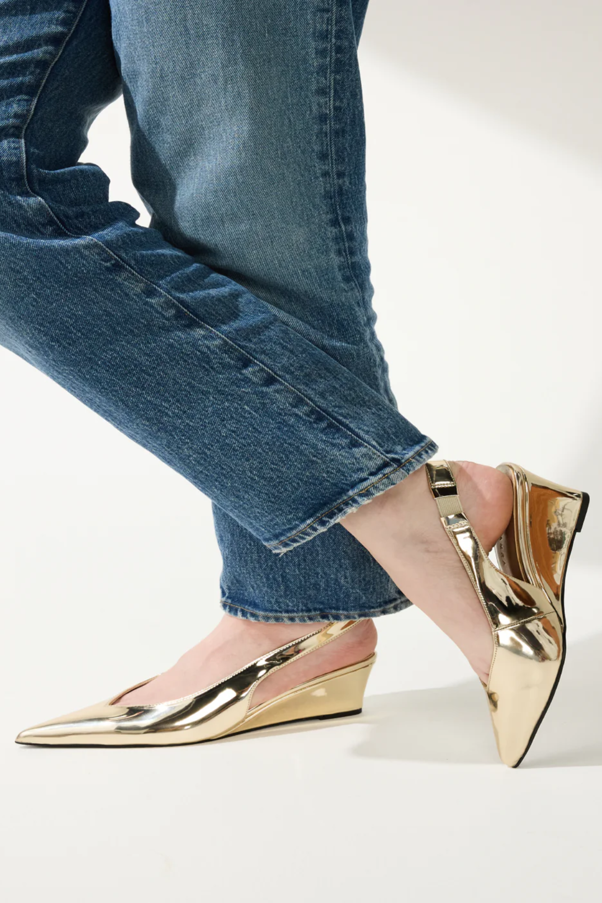 Gold wedge shoes worn with blue jeans on a light background
