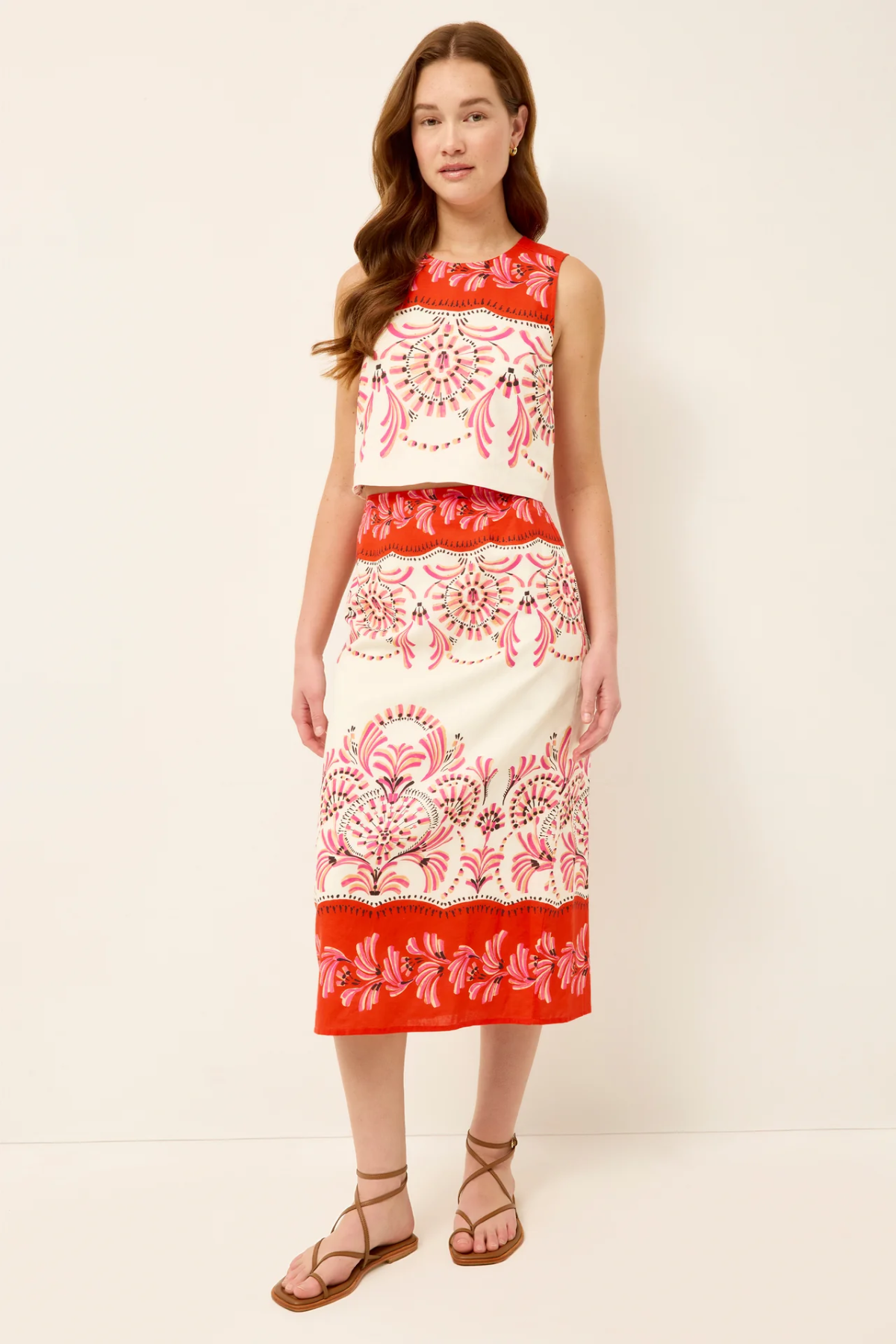 Woman wearing a sleeveless dress with red and white floral pattern on a plain background