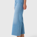 A model wearing light blue cropped flare jeans with a frayed hem, paired with flat slide sandals, shown from the waist down on a light gray studio background.