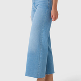 A model wearing light blue cropped flare jeans with a frayed hem, paired with flat slide sandals, shown from the waist down on a light gray studio background.