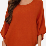 A woman wearing a loose, rust-orange knit top with wide draped sleeves and matching bottoms, shown against a plain light background.