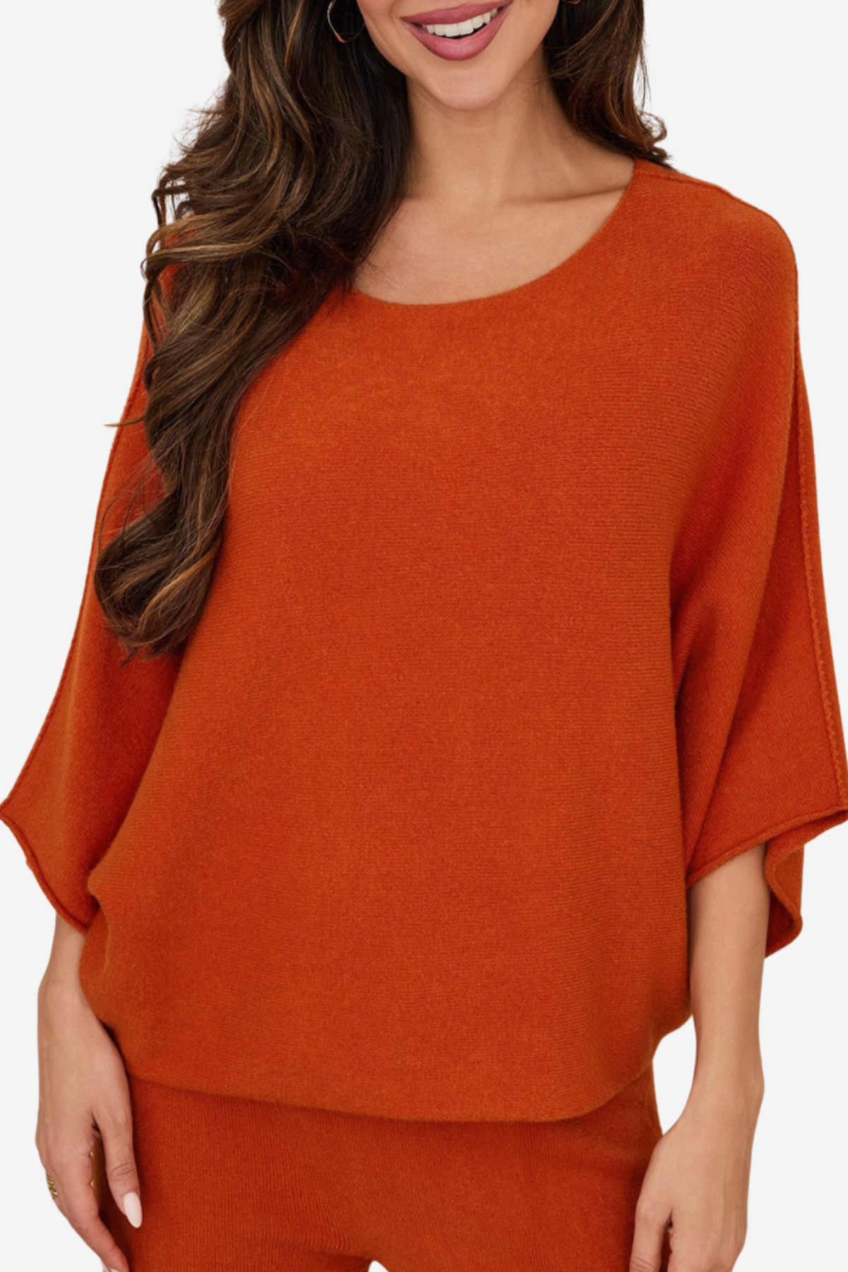 A woman wearing a loose, rust-orange knit top with wide draped sleeves and matching bottoms, shown against a plain light background.