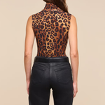A woman shown from the back wearing a sleeveless leopard-print mock neck top and black pants, against a solid beige background.