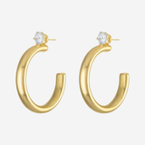 A pair of gold hoop earrings with a small clear round gemstone at the top of each earring, shown on a light gray background.
