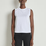 Woman wearing a white sleeveless top with black pants against a plain background