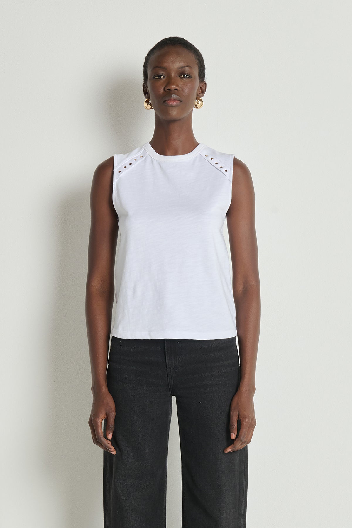 Woman wearing a white sleeveless top with black pants against a plain background