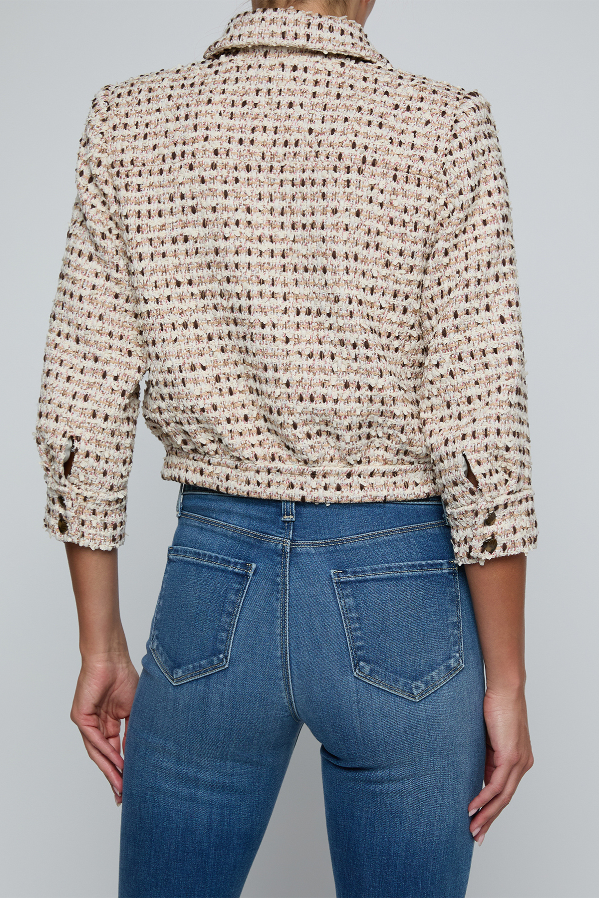 Model wearing a tweed jacket with jeans on and off white background.