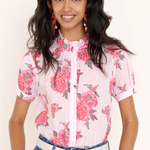 Woman wearing a floral blouse with pink flowers and blue jeans on a plain background