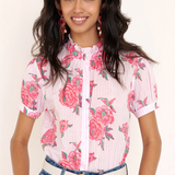 Woman wearing a floral blouse with pink flowers and blue jeans on a plain background