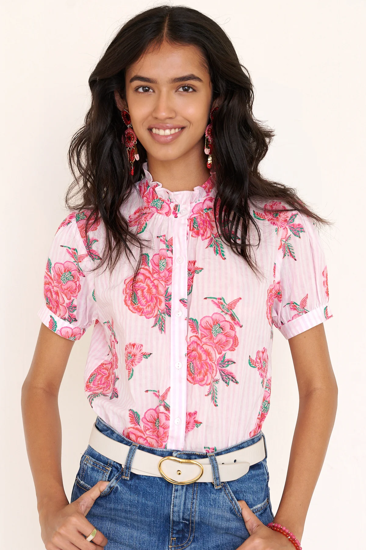 Woman wearing a floral blouse with pink flowers and blue jeans on a plain background
