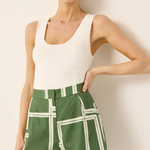 Woman wearing a white tank top and green shorts with white grid pattern against a plain background