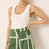 Woman wearing a white tank top and green shorts with white grid pattern against a plain background