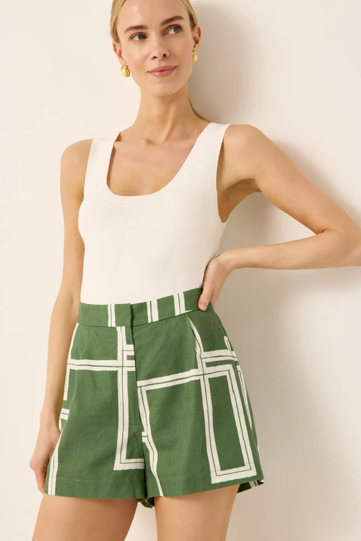 Woman wearing a white tank top and green shorts with white grid pattern against a plain background