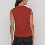 A woman shown from the back wearing a sleeveless rust-red top and dark jeans against a plain light gray studio background.