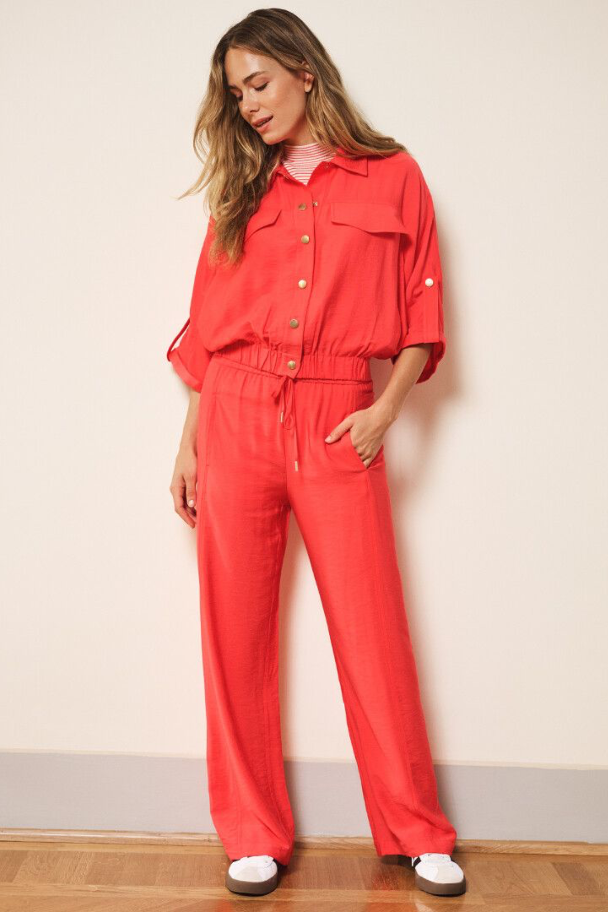 Woman wearing a red set standing against a plain wall.