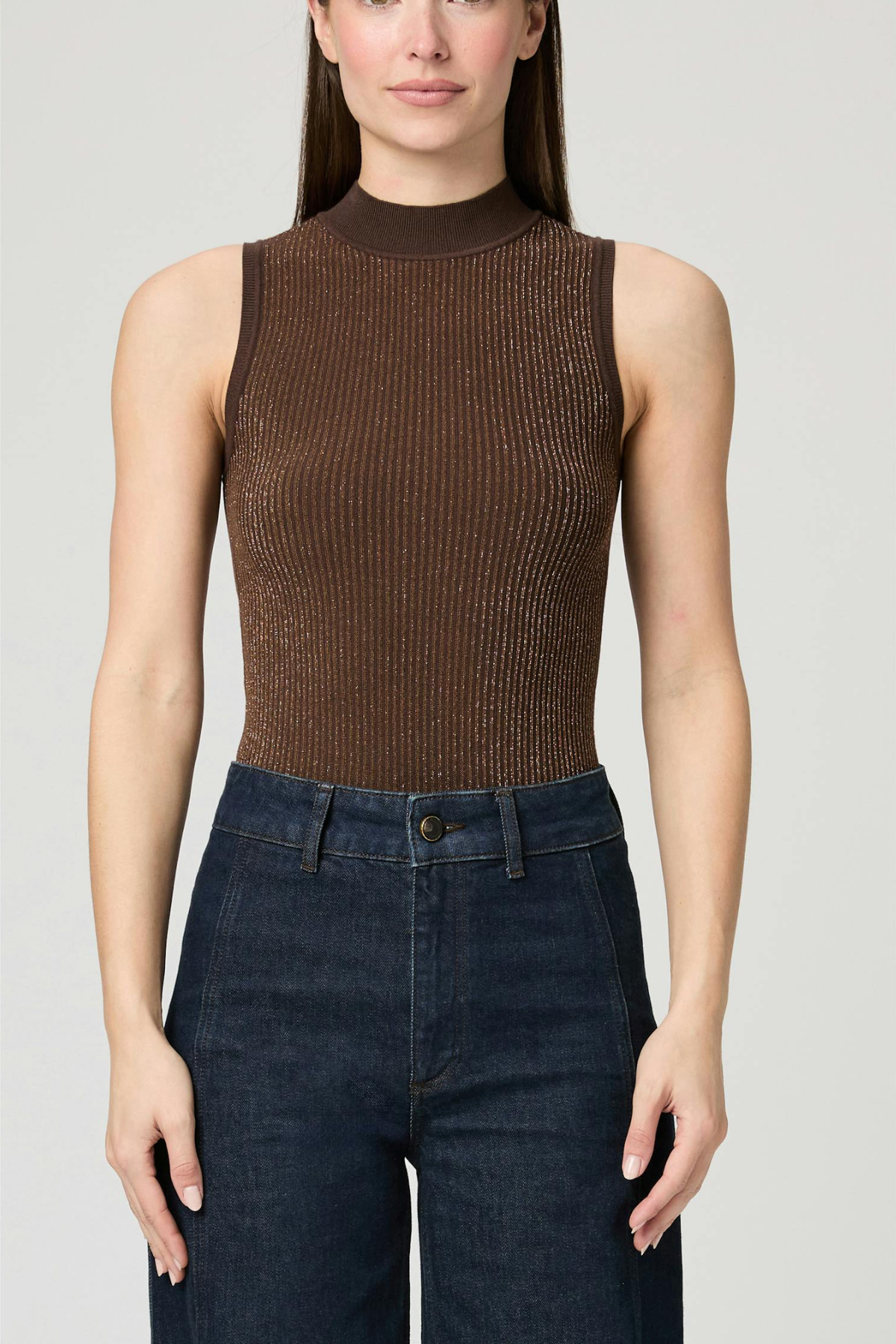 Woman wearing a brown ribbed tank top and dark blue jeans on a light gray background